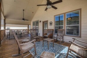 A covered porch with wooden rocking chairs, a ceiling fan, and large windows with blinds.