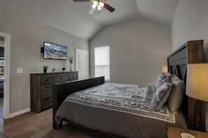 A bedroom with a bed, dresser, TV, and ceiling fan.