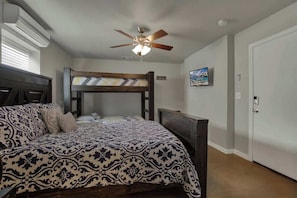 A bedroom with a bunk bed, a ceiling fan, a bed with patterned bedding, a bedside table, and a door.