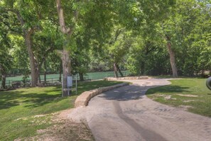 A paved pathway curving through a park with trees and a body of water in the background.