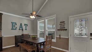 A dining area with a wooden table and chairs, a ceiling fan, and a wall with 'EAT' letters. - Easy Tubing!-Right on the River! (New Braunfels)