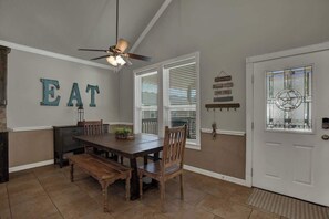 Een eethoek met een houten tafel en stoelen, een plafondventilator en een muur met de letters 'EAT'.