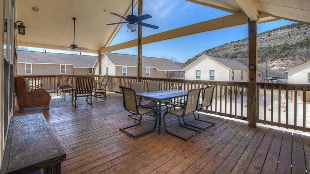 A covered outdoor patio with a table and chairs, a ceiling fan, and a view of neighboring houses. - Easy Tubing!-Right on the River! (New Braunfels)