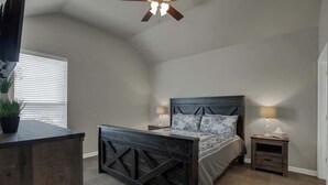 A bedroom with a dark wooden bed frame, two bedside tables with lamps, a ceiling fan, and a window with blinds. - Easy Tubing!-Right on the River! (New Braunfels)