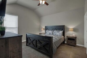 Een slaapkamer met een donker houten bedframe, twee nachtkastjes met lampen, een plafondventilator en een raam met jaloezieën.