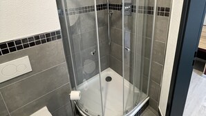 A corner shower with a glass enclosure, a toilet, and tiled walls. - Yebs Hotel (Guenzburg)