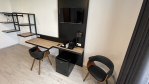 A modern office space with a long desk, two black chairs, a black filing cabinet, and a mounted flat-screen TV. - Yebs Hotel (Guenzburg)