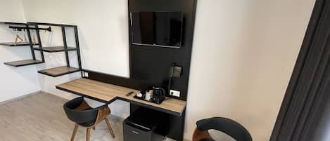 Een moderne kantoorruimte met een lang bureau, twee zwarte stoelen, een zwart archiefkast en een wandgemonteerde flatscreen-tv.