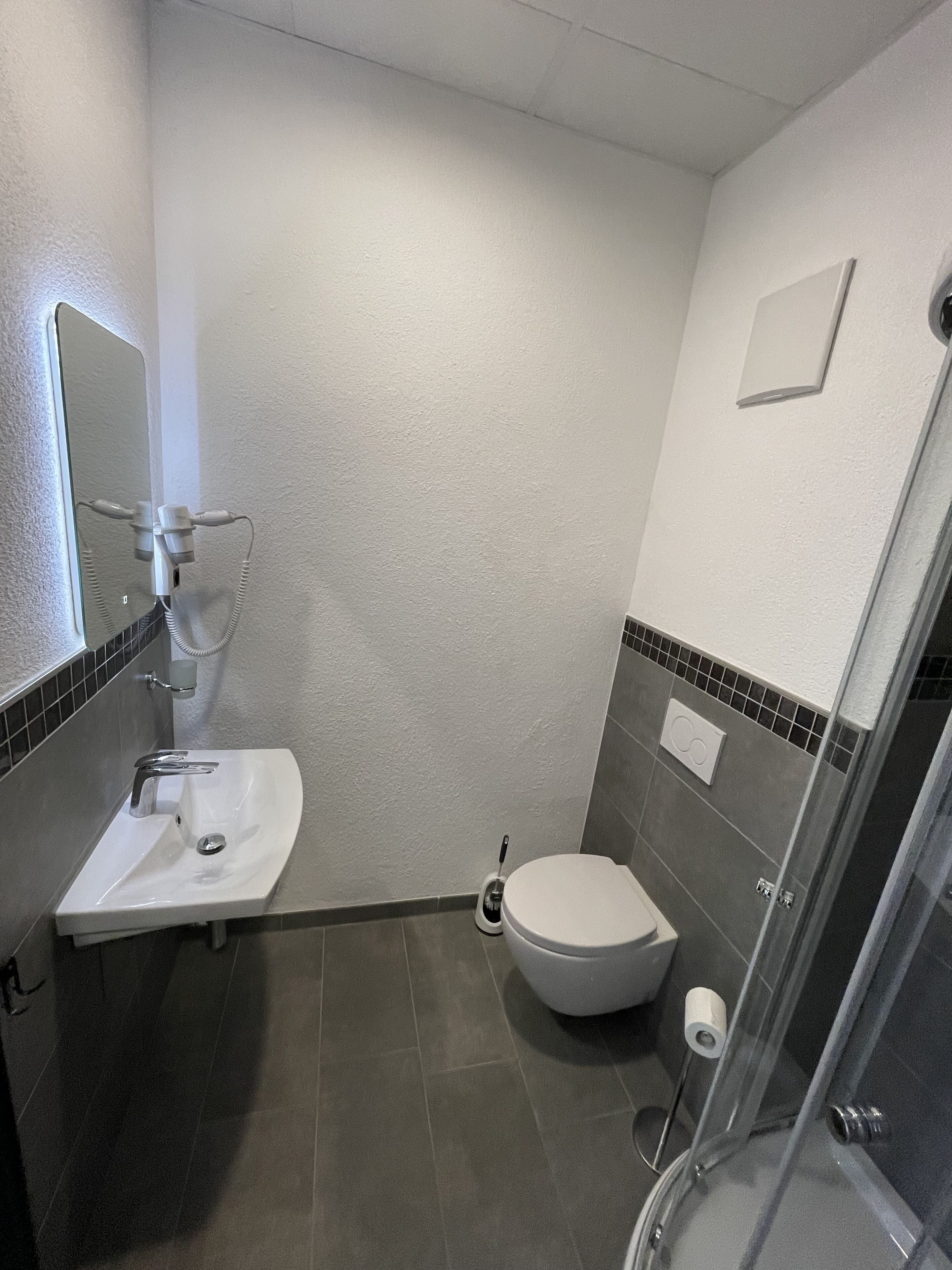 Un baño pequeño con un lavamanos blanco, inodoro y cabina de ducha de vidrio.