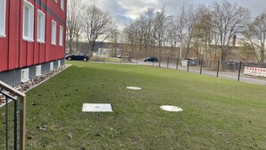 A grassy area with a red building, a fence, and a road with cars. - Yebs Hotel (Guenzburg)