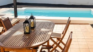 Ein Holztisch mit zwei Laternen und Stühlen, mit Blick auf ein Schwimmbecken.