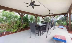 Um pátio externo com mesa, cadeiras, ventiladores de teto e uma pequena mesa para jogos, azul e vermelha.