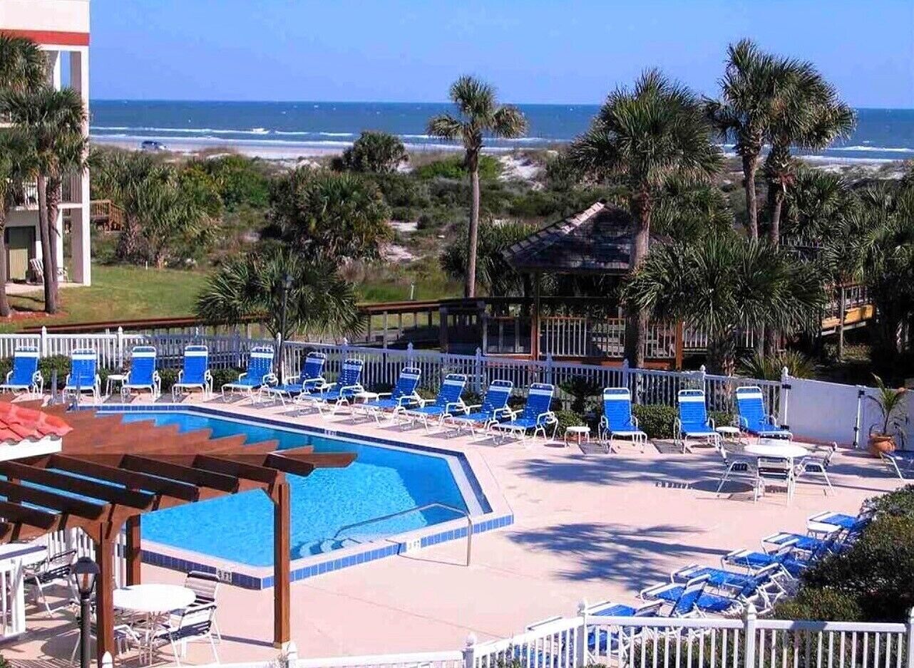 A pool area with blue chairs and a view of the ocean.