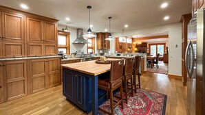 A spacious kitchen with wooden cabinets, a central island with chairs, pendant lighting, and a large refrigerator. - JHRL - Eagles Rest 16 - Newly renovated, spacious townhome (Teton Village)