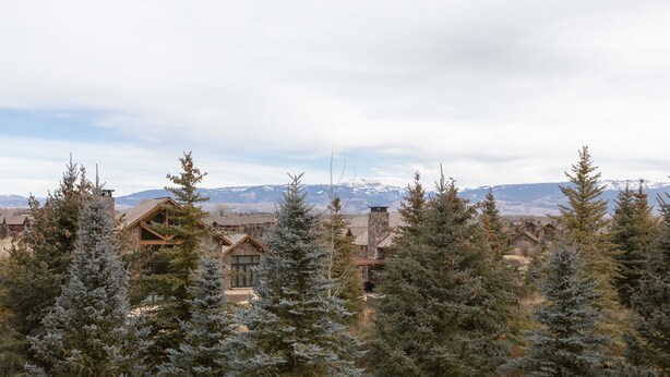A mountain lodge with a stone facade, surrounded by evergreen trees, and a view of snow-capped mountains in the distance. - JHRL - Eagles Rest 16 - Newly renovated, spacious townhome (Teton Village)