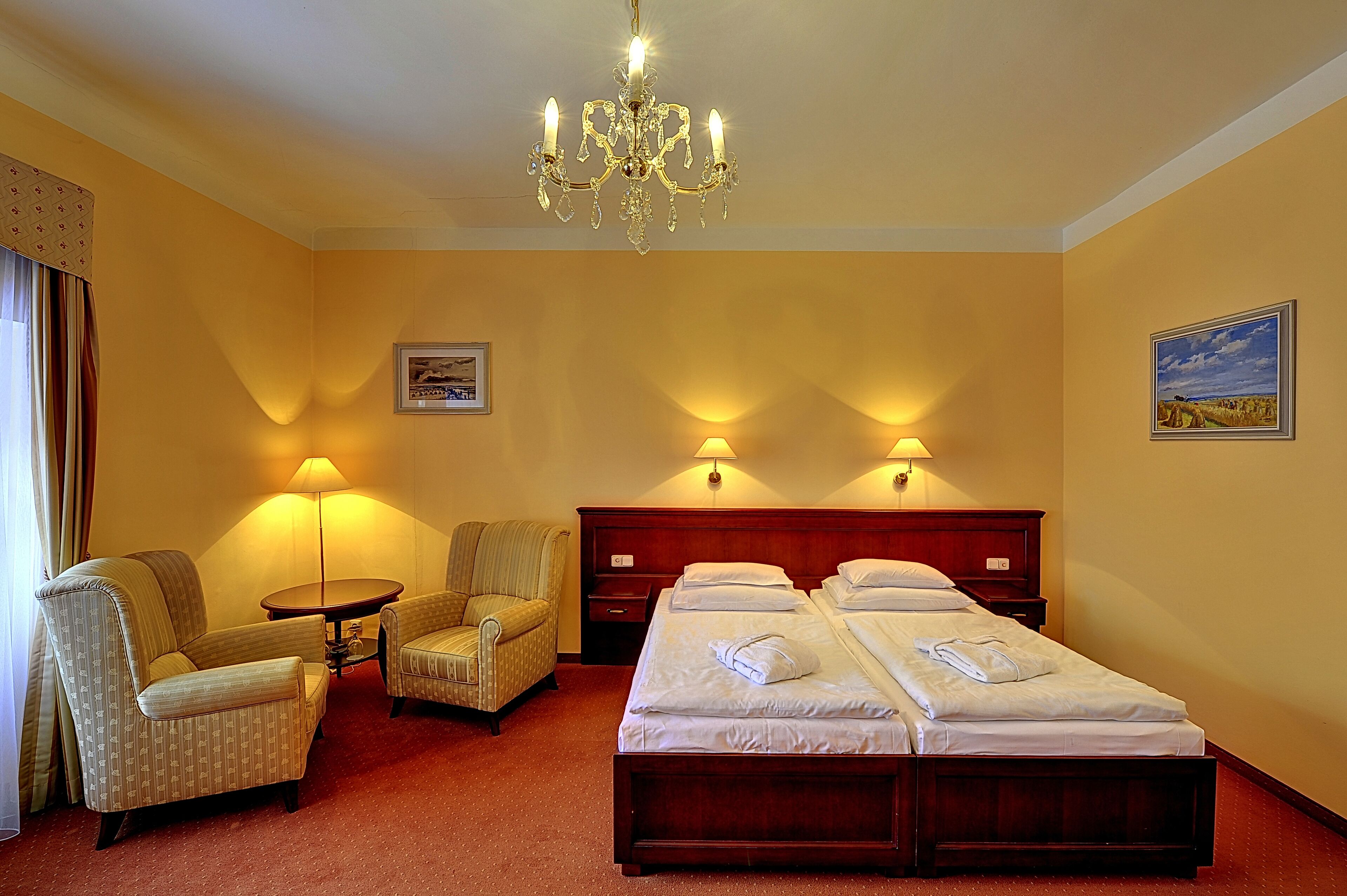 Una habitación de hotel con una cama doble, dos sillones, una mesita y una araña.