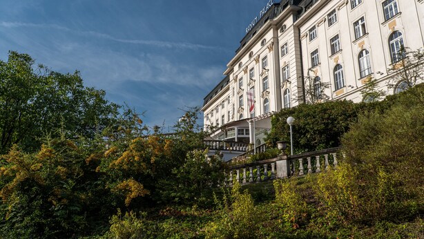 A historic building with classical architecture, a prominent entrance, and a surrounding lush garden. - Hotel Radium Palace (Jachymov)