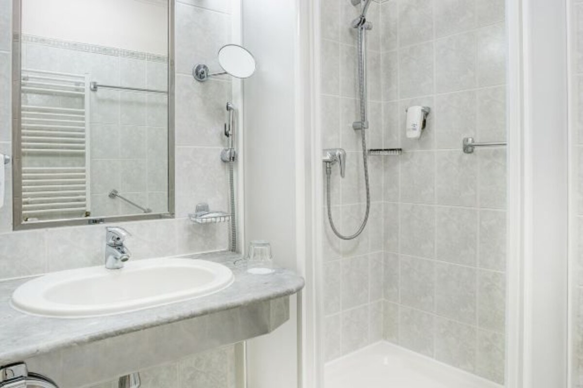 A modern bathroom with a marble sink, a large mirror, a handheld showerhead, and a glass shower enclosure.