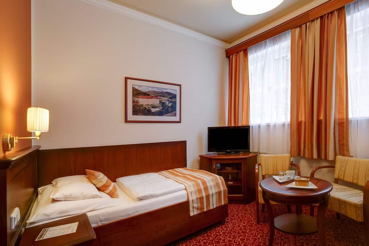 A hotel room with a bed, a television, a small table with a chair, and a window with curtains.