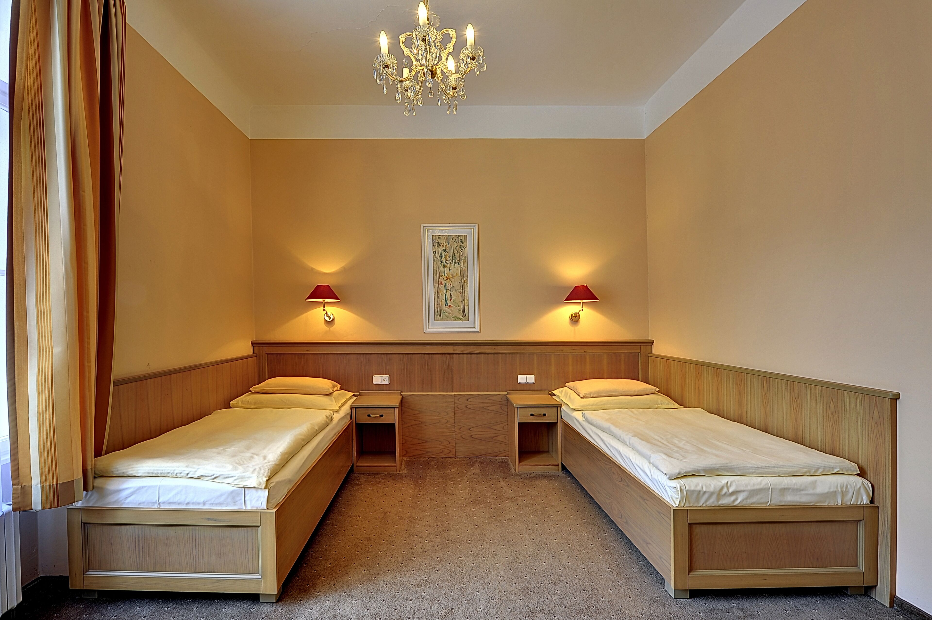 Quarto duplo com duas camas de solteiro, cabeceira de madeira, lustre, luminárias de parede e uma obra de arte emoldurada.