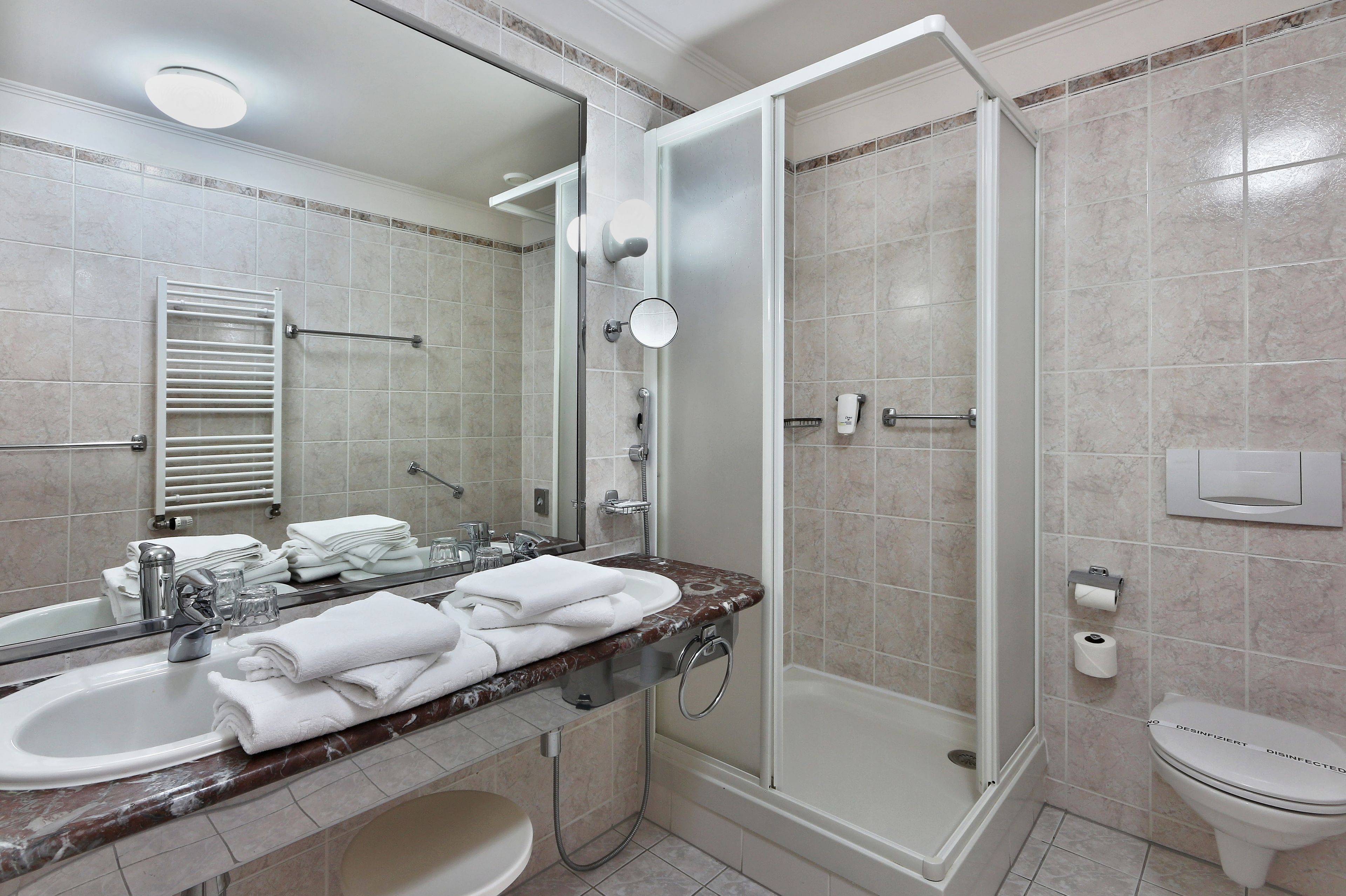 Un baño moderno con cabina de ducha acristalada, tocador con encimera de mármol y un inodoro con etiqueta 'DESINFECTADO'.