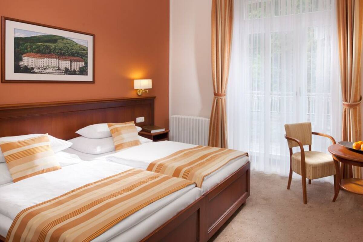 A hotel room with two beds, a sitting area with a table and chairs, and a large window with curtains.