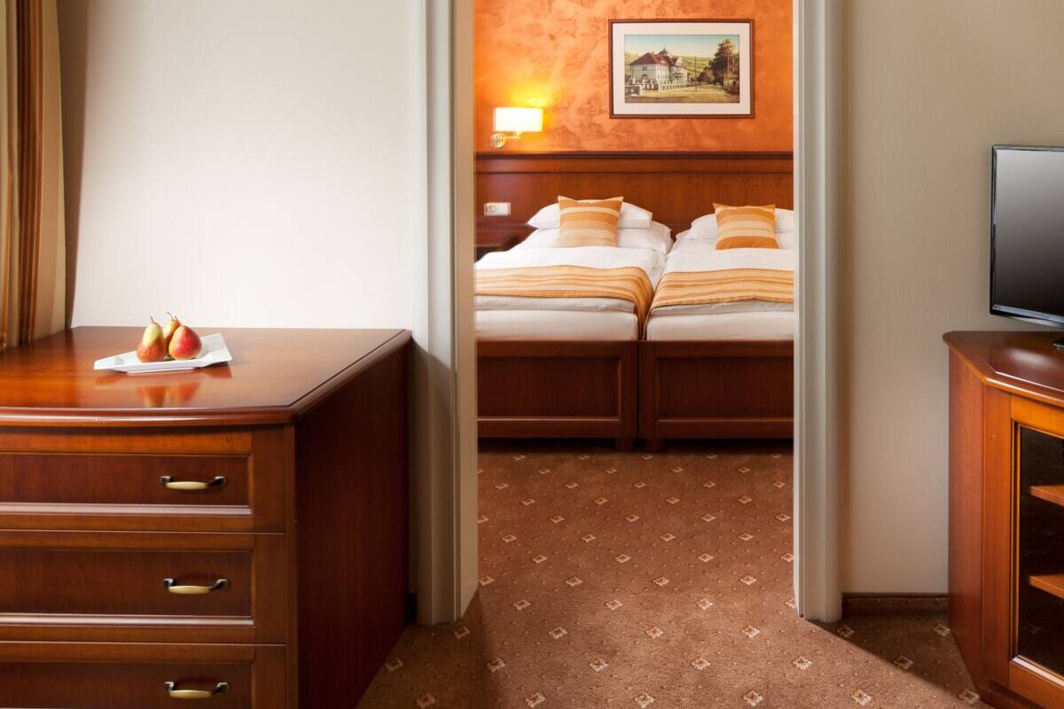 A hotel room with a wooden desk, a television, and two beds with matching pillows.