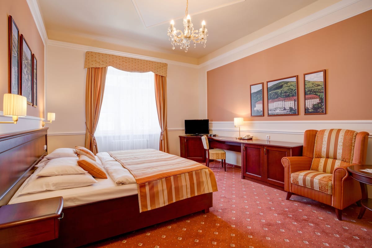 A hotel room with a bed, desk, chair, television, and artwork on the wall.