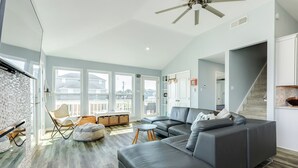 A spacious living room with a large gray sectional sofa, a small round table, and a chair. There are large windows providing natural light and a view of the outside. - Private Beachside Home, Perfect for Families, Updated Interior & Near Beach (Galveston)