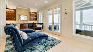 Amplia sala de estar con un sofá azul, puerta de cristal que da a un balcón y una zona de cocina con copas de vino a la vista.