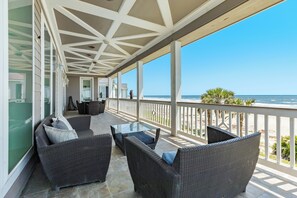 Un espace extérieur aménagé, abrité et doté de mobilier en osier et d’une table en verre, offrant une vue sur la plage.