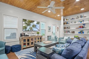 A living room with a wooden ceiling, a ceiling fan, a bookshelf, and a large window with blinds. - `Relax & Unwind: Heated Pool in Gated Community, Just Minutes from Town and Beach (Port Aransas)