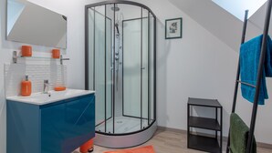 Un baño moderno con cabina de ducha de vidrio, tocador azul y estante negro.