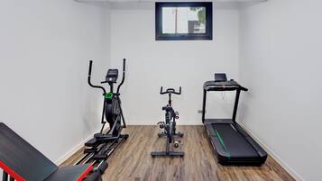 Una habitación pequeña y bien iluminada con una cinta caminadora, una elíptica y un banco.