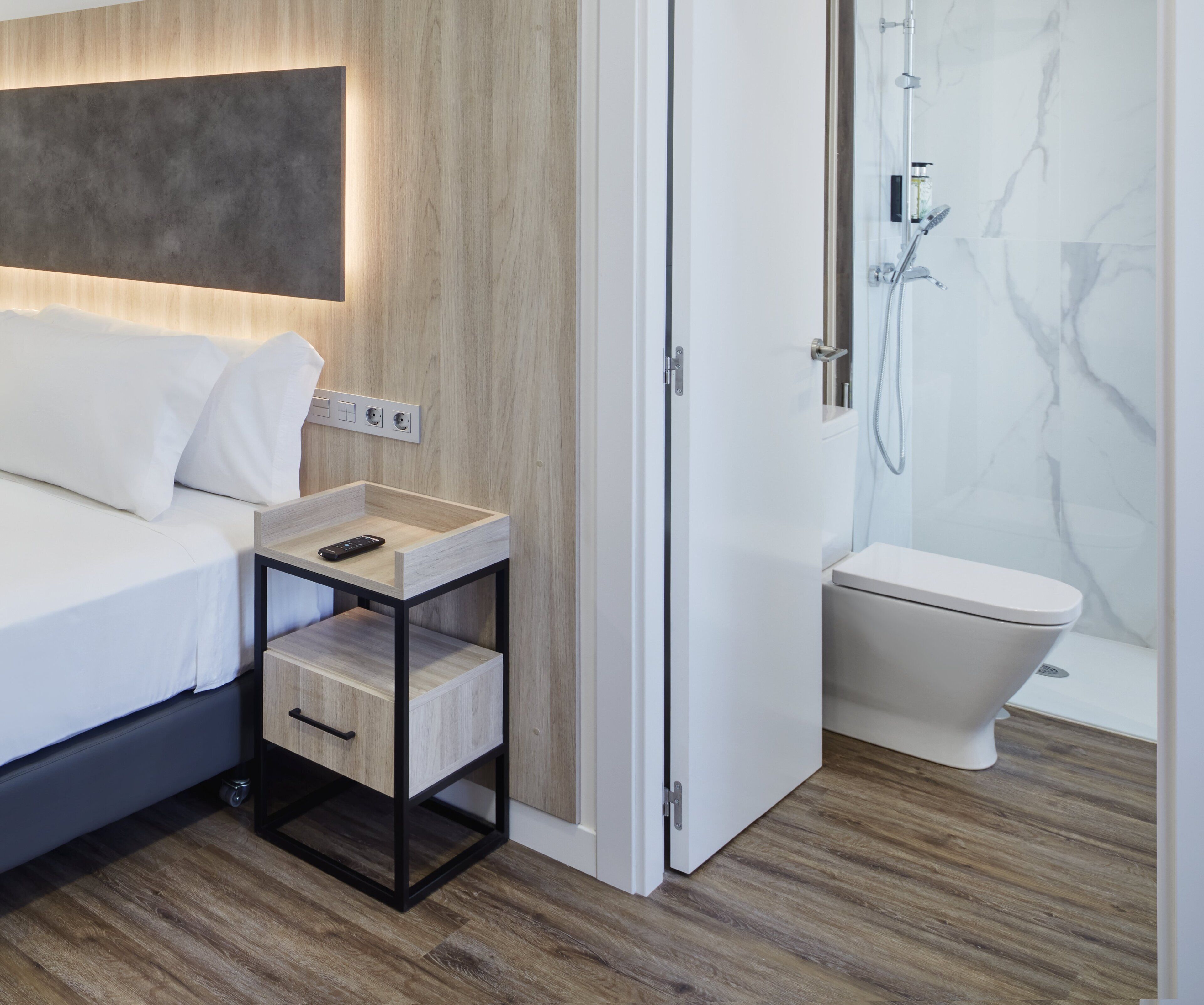 A modern bathroom with a shower, toilet, and bedside table with a remote control.