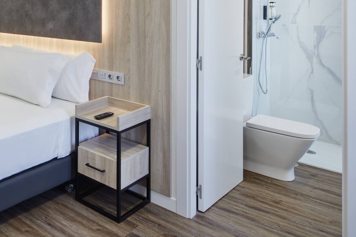 Un baño moderno con ducha, inodoro y mesita de noche con control remoto.