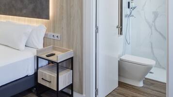 A modern bathroom with a shower, toilet, and bedside table with a remote control.