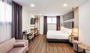 Una habitación de hotel moderna con una cama, un escritorio, una silla, un sofá y una pequeña mesa redonda.