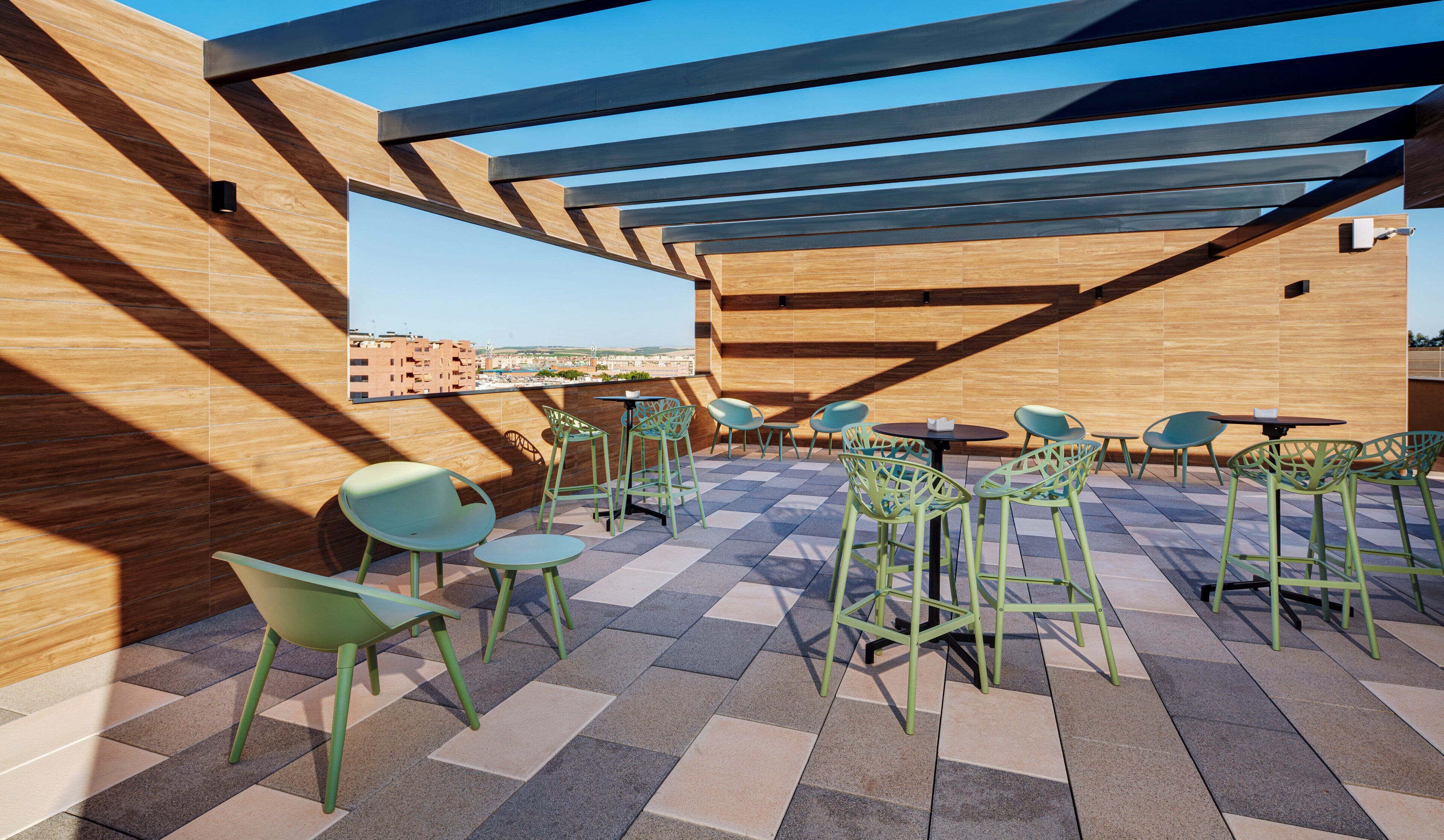 Una terraza en la azotea con suelo de madera, sillas verdes y vistas a la ciudad.