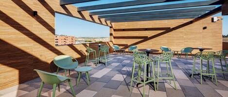 Una terraza en la azotea con suelo de madera, sillas verdes y vistas a la ciudad.
