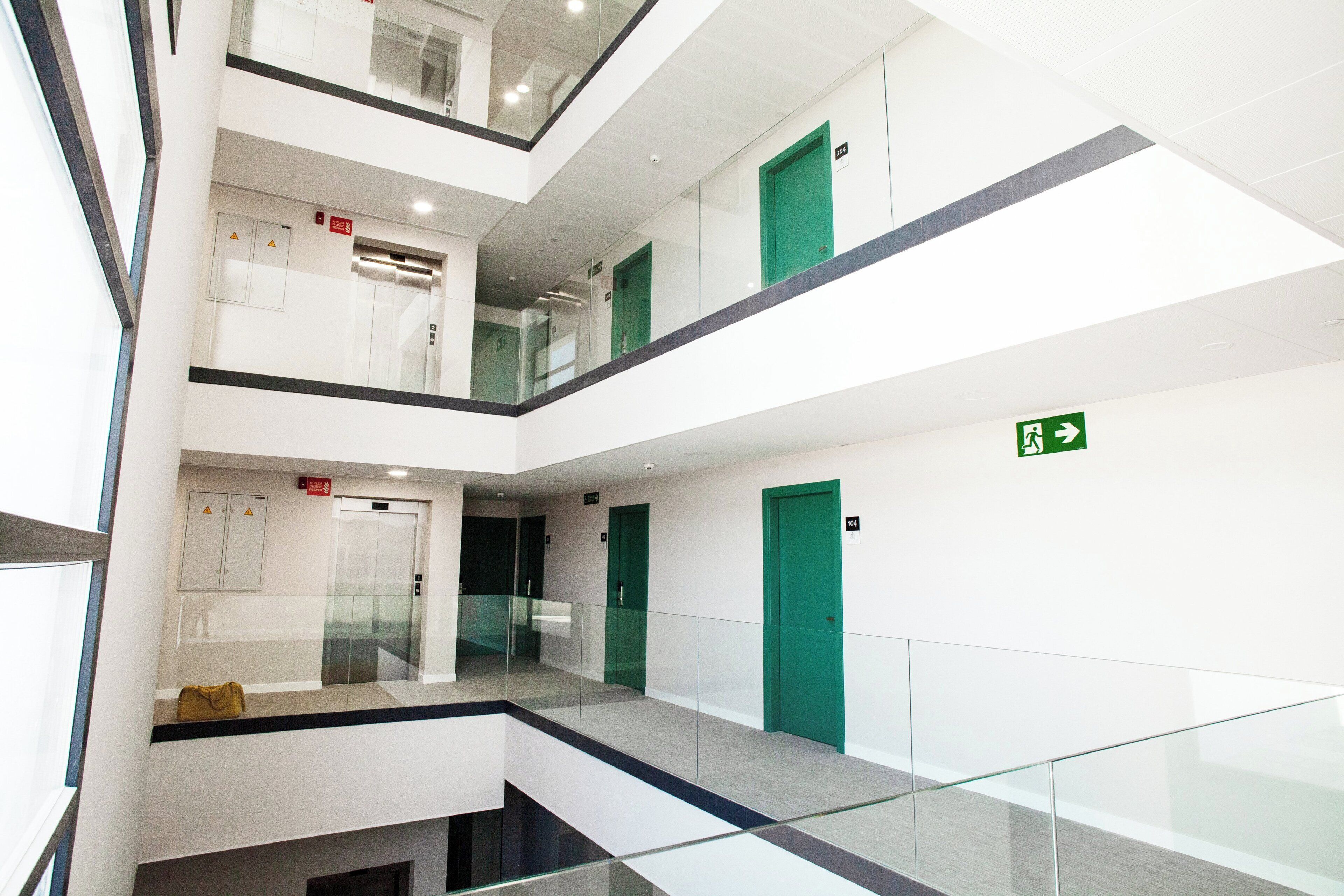 A multi-level interior with glass railings, green doors, and a visible emergency exit sign.