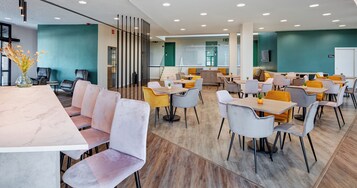 A modern dining area with multiple tables and chairs, a central seating area, and a staircase leading to an upper level.