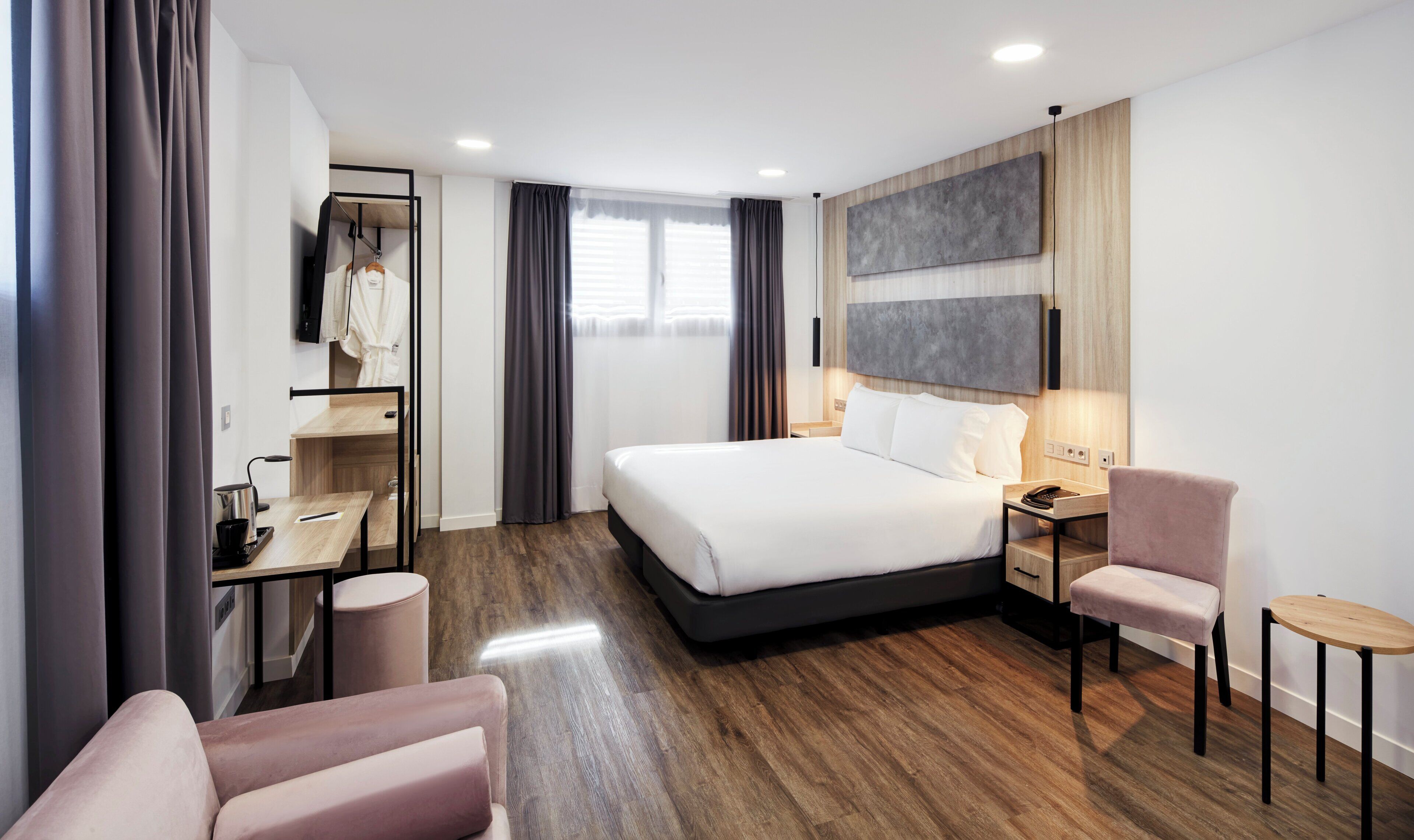 A modern hotel room with a large bed, a desk with a chair, a small seating area, and a TV mounted on the wall.
