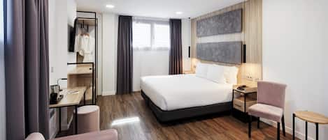 Een moderne hotelkamer met een groot bed, een bureau met stoel, een zithoekje en een aan de muur bevestigde televisie.