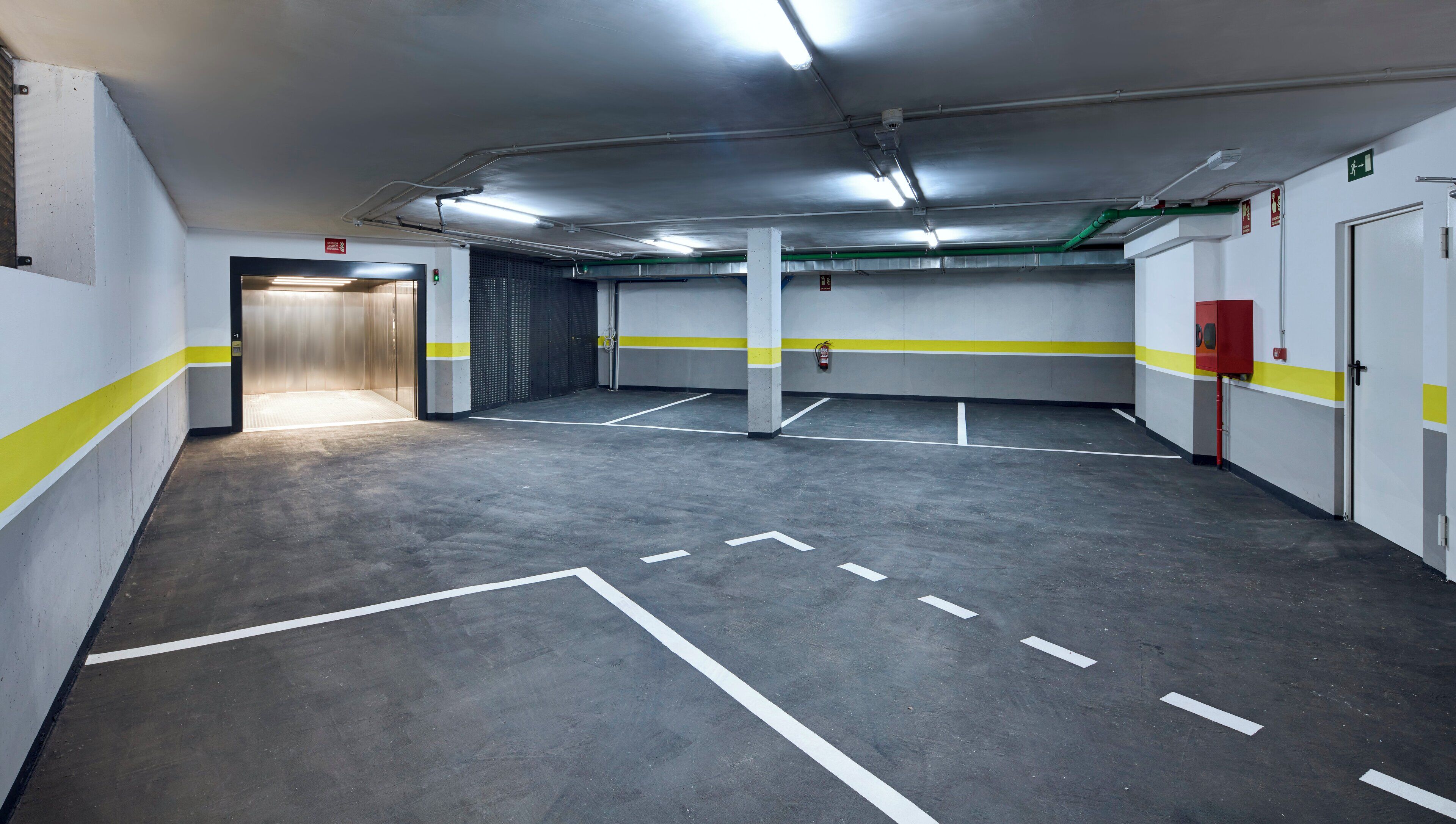 Een parkeergarage met diverse parkeerplaatsen, markeringen op de vloer en een brandblusser aan de muur.