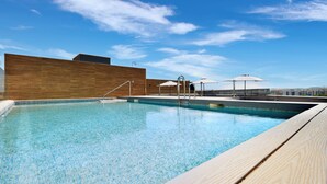 Ein Schwimmbecken mit klarem, blauem Wasser, einer Holzterrasse und Sonnenschirmen.