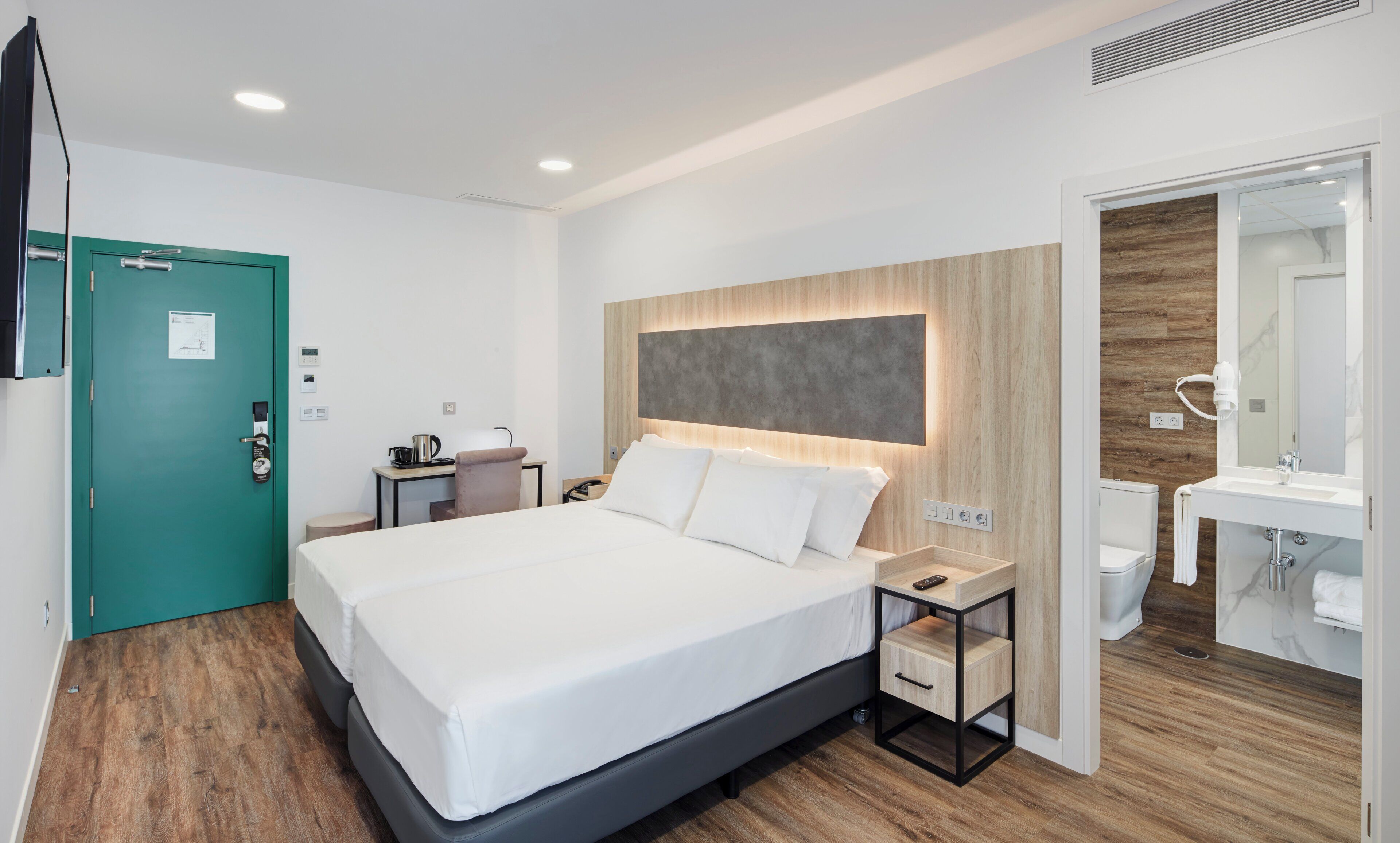 A modern hotel room with a large bed, bedside tables, a desk, and a bathroom.