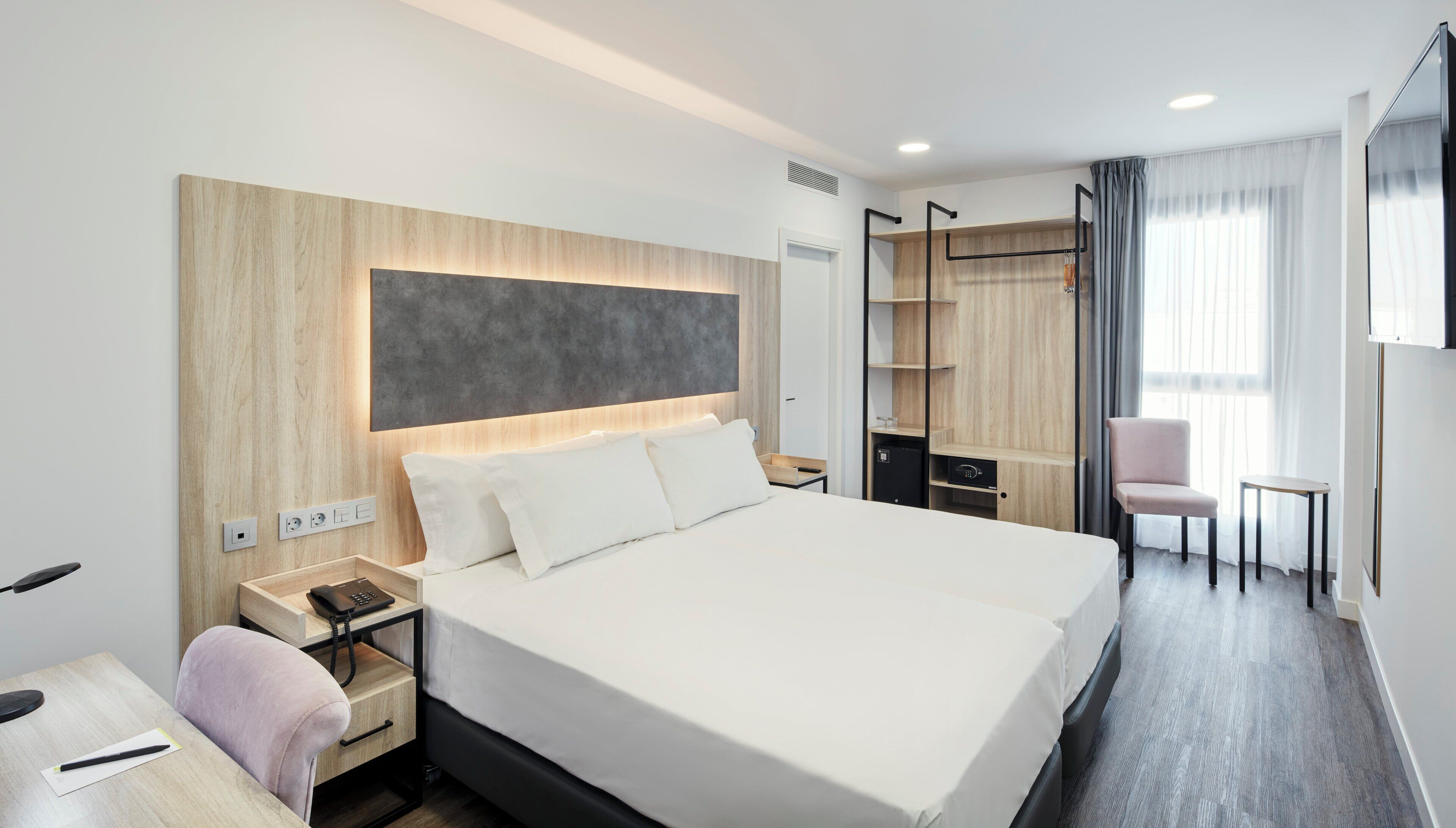 Una habitación de hotel moderna con una cama grande, mesitas de noche, un escritorio, una silla y un armario.