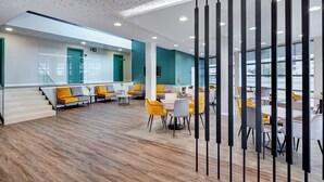 Un área de espera moderna con asientos, una escalera y vistas al exterior.