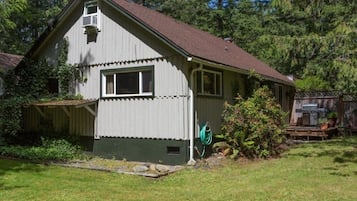 Cozy home with a front porch, surrounded by a well-manicured lawn and a deck with a barbecue grill.
